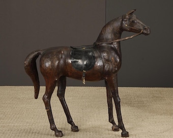 May include: A dark brown horse sculpture with a black saddle and bridle. The horse is standing on a light-colored rug. The sculpture is made of a material that appears to be leather or a similar material. The horse is a decorative item.