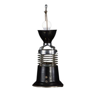 May include: A vintage-style pendant light fixture with a black and silver finish. The light has a bulb, a black conical shade, and a cylindrical base with horizontal bars. The fixture is suspended by a cord and a metal rod.