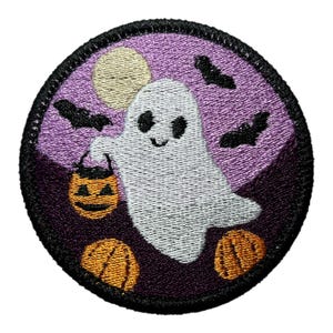 May include: Embroidered Halloween patch featuring a friendly ghost holding a jack-o'-lantern. The design includes bats, pumpkins, and a full moon against a purple and black background. The patch is round with a black border.