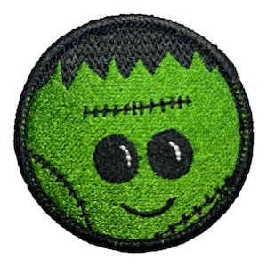 May include: Round embroidered patch depicting a green Frankenstein monster face with black hair and stitched details. The patch has a smiling mouth and a black border, suitable for Halloween or monster-themed projects.