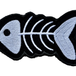 May include: Embroidered patch with a fish skeleton design. The patch has a black border and a light blue fish skeleton. The design is a simple, yet eye-catching, representation of a fish's skeletal structure.