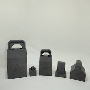 May include: Five gray 3D printed boxes with a flower design. The boxes are different sizes and shapes. The largest box is a rectangular box with a handle on top. The other boxes are smaller and have different shapes.