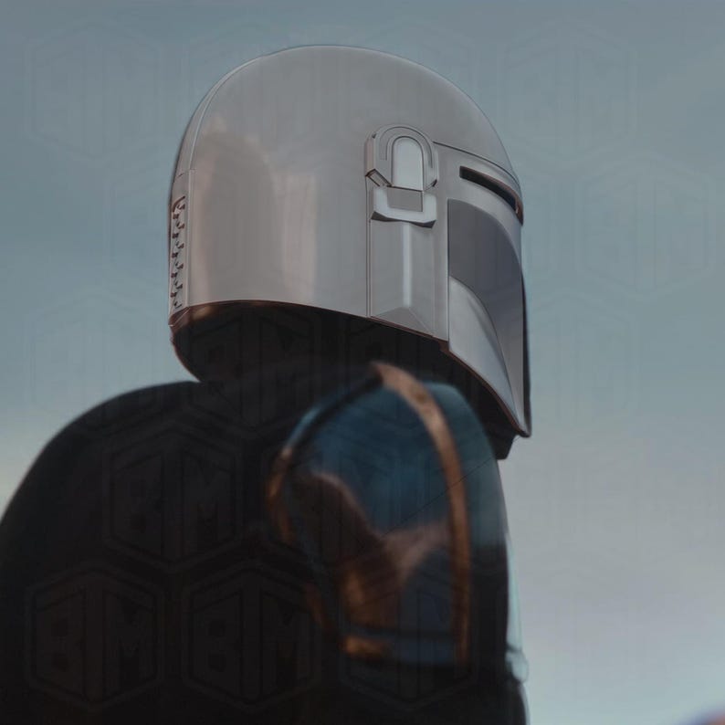 May include: A silver Mandalorian helmet with a dark visor and a distinctive T-shaped opening. The helmet is part of a suit of armor, with blue and gold accents visible on the shoulder. The image is a close-up, focusing on the helmet's details.