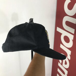 May include: Black baseball cap with a flat brim. The cap features a colorful embroidered design on the side. The cap is made of a durable fabric and has a structured fit. The brim is dark and the cap is a solid black color.