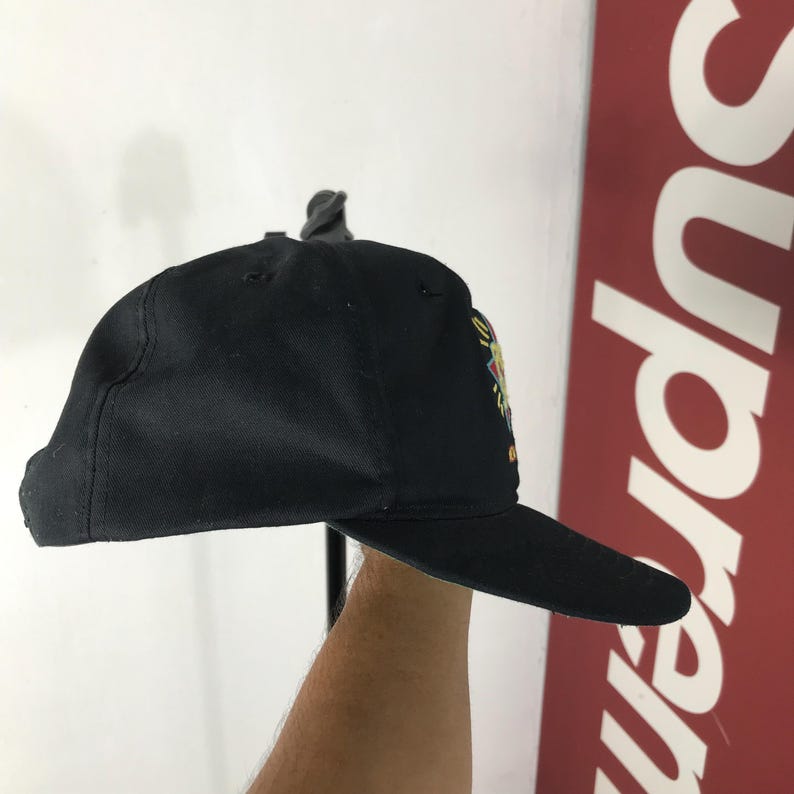 May include: Black baseball cap with a flat brim. The cap features a colorful embroidered design on the side. The cap is made of a durable fabric and has a structured fit. The brim is dark and the cap is a solid black color.
