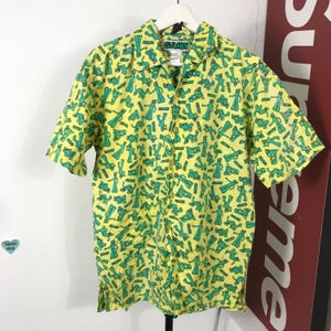 May include: Yellow button-down shirt with a green Gumby character pattern. The shirt has short sleeves and a collar. The tag on the collar reads "GUMBY".