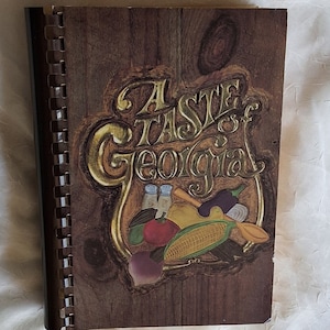 May include: A brown cookbook with a gold embossed title "A Taste of Georgia" and a colorful illustration of vegetables and spices.
