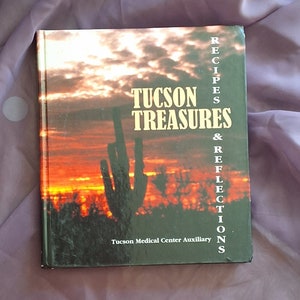 May include: A book titled "Tucson Treasures & Reflections" with a sunset and a saguaro cactus on the cover. The book is published by the Tucson Medical Center Auxiliary.