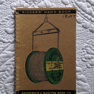 May include: Vintage "Riggers' Hand Book" with a brown cover and spiral binding. The cover features a green and yellow illustration of a cable spool suspended by chains. The text includes "Broderick & Bascom Rope Co."