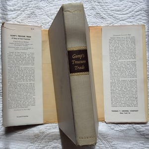 May include: A vintage book titled "Gump's Treasure Trade" by Carol Green Wilson. The book has a light beige cover with a dark brown label and gold lettering. The book is open, revealing pages with text and a title page.