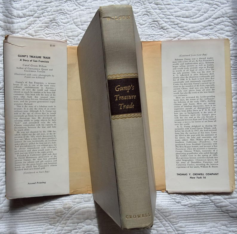 May include: A vintage book titled "Gump's Treasure Trade" by Carol Green Wilson. The book has a light beige cover with a dark brown label and gold lettering. The book is open, revealing pages with text and a title page.