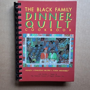 May include: A red cookbook titled "The Black Family Dinner Quilt Cookbook" with black spiral binding. The cover features text in yellow and green, and an illustration of people at a table. The book includes the text "Health Conscious Recipes & Food Memories".