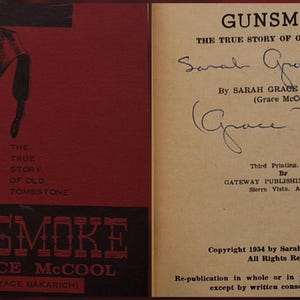 May include: Open book titled "Gunsmoke" by Grace McCool. The cover is red with a black illustration of a gun and holster. The title and author's name are in white. The right page has handwritten signatures.