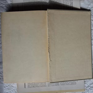 May include: An open book with aged, off-white pages. The binding is visible, showing the rough edges of the pages. Additional pages with text are partially visible, suggesting a vintage or antique book.