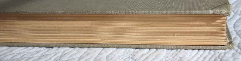 May include: Close-up of a vintage book with a faded green cover and aged, yellowed pages. The book's spine is visible, showing the binding and the texture of the cover material. The pages are slightly uneven, indicating age.
