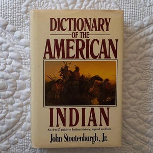 May include: A book cover with a brown background and the title "Dictionary of the American Indian" in red lettering. The cover features a painting of Native Americans on horseback.