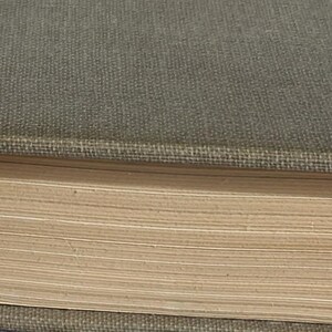 May include: Close-up of a vintage book with a muted green cover and aged, yellowed pages. The book's spine and corners show signs of wear, suggesting its age. The pages are slightly fanned out, revealing their texture.