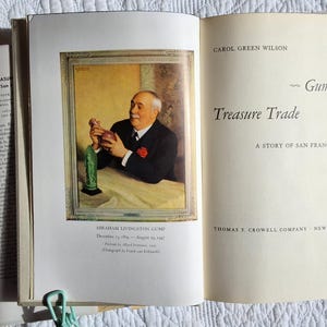 May include: Open book with a portrait of Abraham Livingston Gump holding a decorative object. The book's title is "Gump's Treasure Trade: A Story of San Francisco" by Carol Green Wilson. The book is open to a page with text.