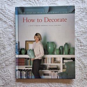 May include: A book titled "How to Decorate" by Martha Stewart Living. The cover features a woman holding a vase and a bookshelf with decorative items.