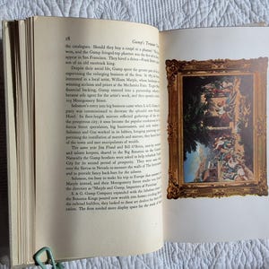 May include: An open book with text on the left page and a framed painting on the right. The painting has a gold frame and depicts a scene with figures and architectural elements. A green paper clip holds the pages together.