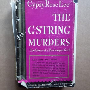 May include: A vintage paperback book titled "The G-String Murders" by Gypsy Rose Lee. The cover is a vibrant magenta with white lettering. The book's cover has some wear and tear, with the text "The Story of a Burlesque Girl".