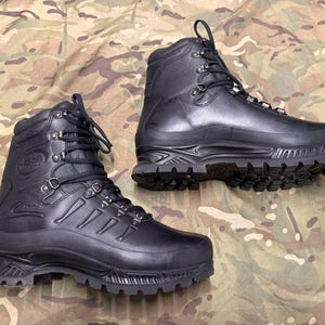 Könnte beinhalten: Ein Paar schwarze Lederstiefel mit hohem Schaft, robuster Gummilaufsohle, verstärkten Zehenkappen und Metallösen für die schwarzen Schnürsenkel. Die Stiefel verfügen über einen gepolsterten Schaftrand und ein strukturiertes Design mit Nähten.