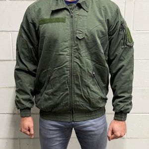 Peut inclure: Un blouson bomber vert olive doté d'une fermeture éclair intégrale sur le devant, d'un col rabattu, ainsi que de poignets et d'un ourlet côtelés. Il comprend deux poches zippées à la taille, une poche poitrine verticale et des bandes auto-agrippantes.