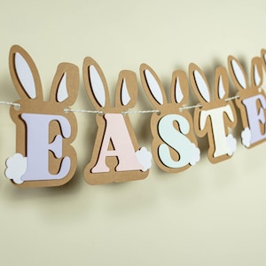 May include: A brown paper Easter banner with the word "Easter" in pastel colours. Each letter has bunny ears and a white fluffy tail.