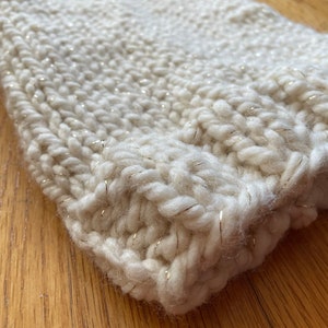 May include: A close-up of a white knitted fabric with gold thread woven throughout. The fabric is soft and fluffy, and the gold thread adds a touch of sparkle.