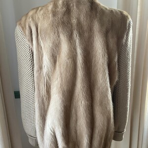 May include: A beige fur bomber jacket with knitted sleeves. The jacket has a ribbed collar and cuffs.