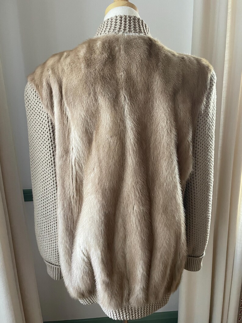 May include: A beige fur bomber jacket with knitted sleeves. The jacket has a ribbed collar and cuffs.
