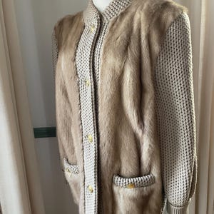 May include: A beige knitted cardigan with fur panels on the front and sleeves. The cardigan has a button closure and two pockets.