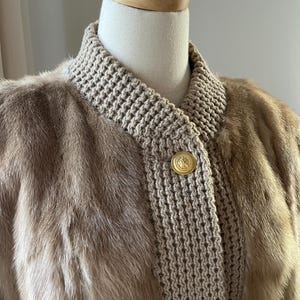 May include: A brown fur jacket with a knitted collar and gold buttons. The jacket is on a white mannequin.