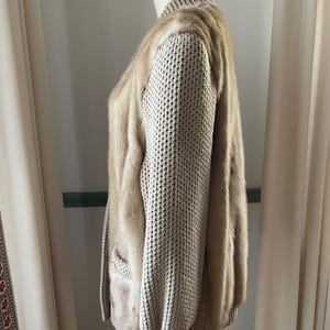May include: A beige knitted cardigan with a fur trim. The cardigan has a long sleeve and a ribbed knit texture.