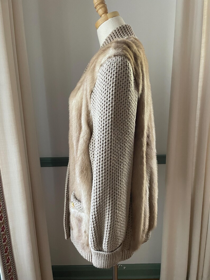 May include: A beige knitted cardigan with a fur trim. The cardigan has a long sleeve and a ribbed knit texture.
