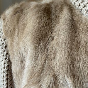 May include: Close-up of a light brown fur fabric. The fur is soft and fluffy, with a subtle sheen.