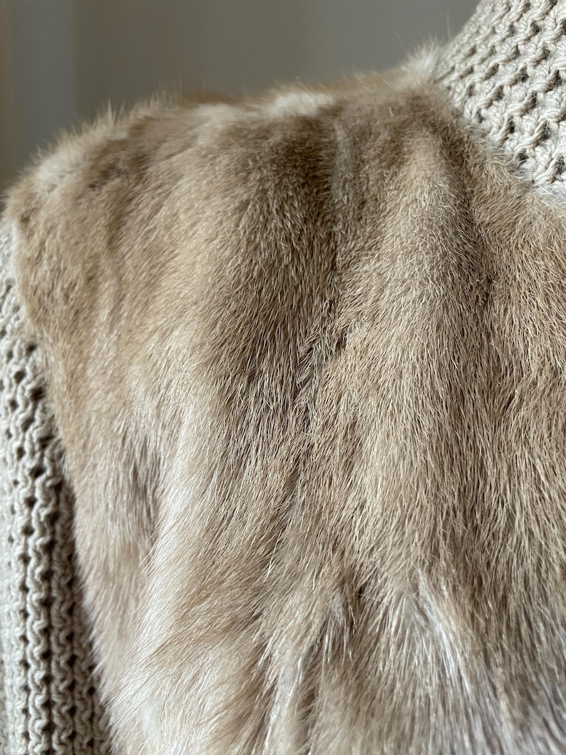 May include: Close-up of a light brown fur fabric. The fur is soft and fluffy, with a subtle sheen.