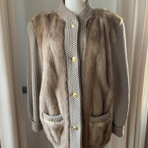 May include: A beige knitted cardigan with fur detailing on the front and sleeves. The cardigan has a button closure and two pockets.