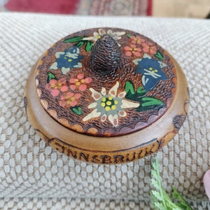 May include: A wooden trinket box with a carved wooden lid featuring painted flowers and the word "Innsbruck".