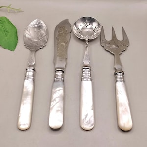 May include: A collection of four antique serving implements. The set comprises a spoon, knife, ladle, and fork. Each item features a silver-coloured metal head with detailed patterns and a white, pearlescent handle. The handles are approximately 10 cm long.