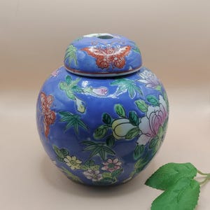 May include: A blue ceramic ginger jar with a matching lid. The jar is decorated with colorful floral and butterfly motifs. The lid features a butterfly design. The jar has a round shape and is likely used for storage or decoration.