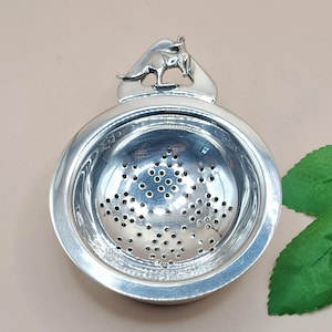 May include: A silver tea infuser with a kangaroo figure on top. The infuser has a round bowl shape with small holes for steeping tea leaves. The kangaroo is in a leaping pose, adding a decorative touch to the tea accessory.