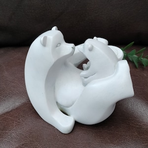May include: White ceramic sculpture of two polar bears, one larger than the other, with the smaller bear nestled in the larger bear's arms. The bears are in a hugging pose.
