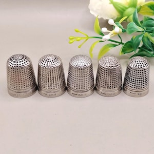 May include: Five silver thimbles with detailed patterns. Each thimble features a unique design on the top and sides, with "PAT.G" stamped on the base. The thimbles are displayed in a row, highlighting their intricate craftsmanship and design.