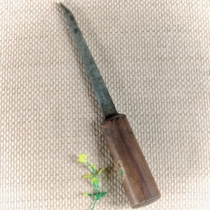 May include: A hand tool featuring a long, slender, dark grey metal spike with a pointed tip and a cylindrical wooden handle. The metal shaft shows signs of oxidation and wear, while the wooden handle has a smooth, polished brown finish.