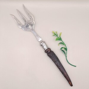Könnte beinhalten: Eine antike Serviergabel mit drei Zinken und aufwendigen floralen Details am Silberkopf. Der Griff besteht aus dunkelbraunem Geweih und silbernen Akzenten. Ein dekoratives Stück zum Servieren.