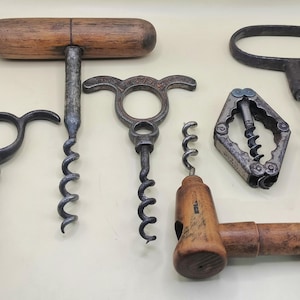 May include: Collection of antique corkscrews in various designs. Includes corkscrews with wooden handles, metal handles, and unique shapes. The corkscrews are made of metal and wood, showcasing a range of styles and ages.