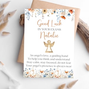 May include: A greeting card with the words "Good Luck in Your Exams Natalie" in a decorative font. The card features a gold angel figurine and floral accents in orange, blue, and white. A message of support is printed below.