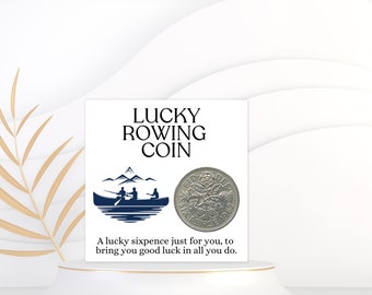May include: A white card with blue text that reads "Lucky Rowing Coin". The card features a blue illustration of two people rowing a boat. A silver sixpence coin is on the card. The text on the card reads "A lucky sixpence just for you, to bring you good luck in all you do."