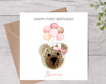 May include: A square greeting card with a crocheted teddy bear face holding watercolor balloons. The card reads "HAPPY FIRST BIRTHDAY" and "Bonnie" in pink script. The card is on a wooden surface.